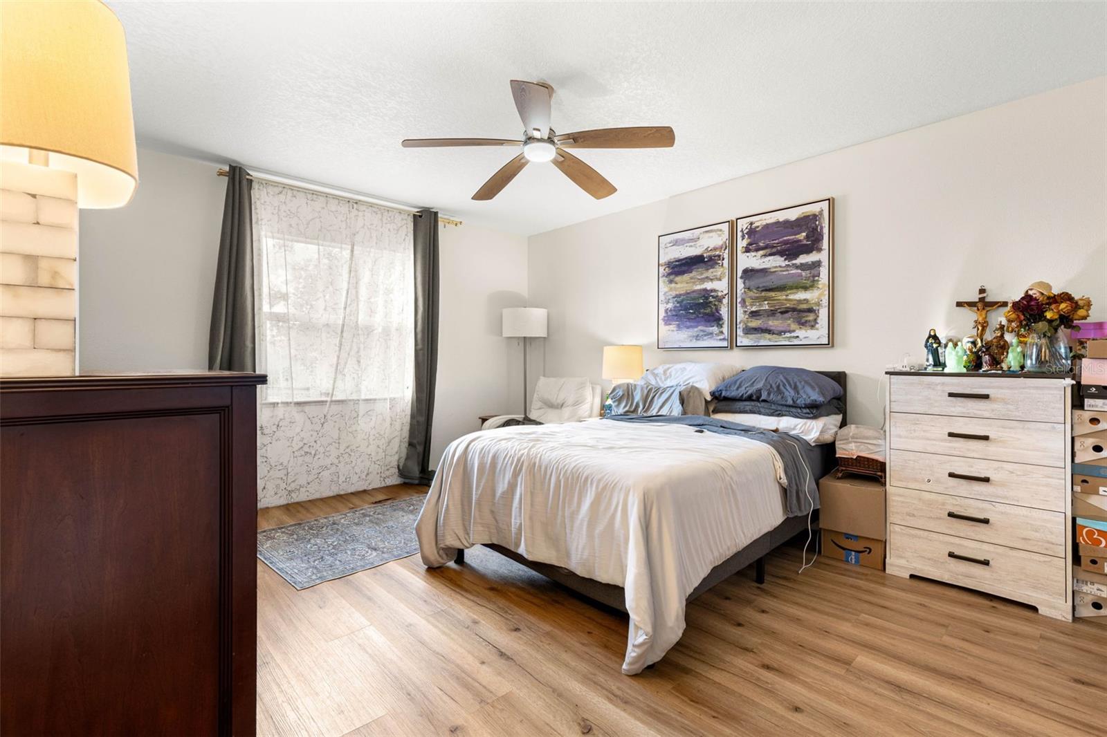 Bedroom three offers a generously proportioned layout with warm wood-look luxury vinyl flooring, a contemporary ceiling fan, neutral walls, and a large window that welcomes natural light. Plenty of room for a full bedroom furniture arrangement without feeling crowded.