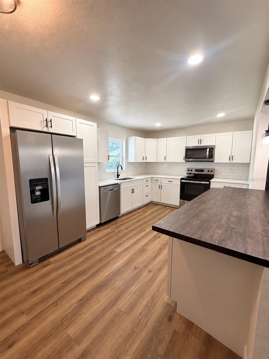 Updated kitchen featuring white shaker-style cabinetry, stainless steel appliances, subway tile backsplash, and expansive countertop space.