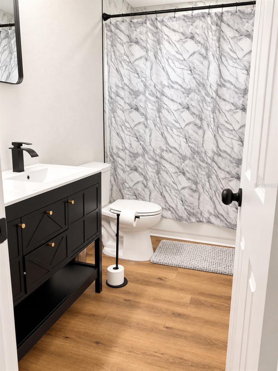 Updated bathroom featuring a, garden tub, contemporary black vanity, white countertop, and modern fixtures.