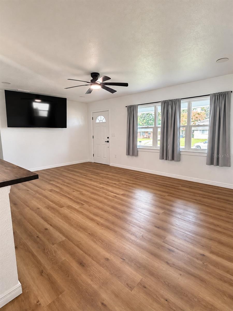 Bright and spacious living room featuring updated wood-look flooring, ceiling fan, and multiple windows providing natural light.