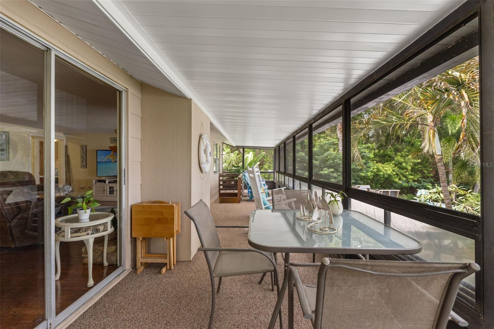 Outdoor dining with a tropical backdrop! This spacious screened porch offers room for a dining table and additional seating, making it an inviting extension of the upper-level living area. Sliding glass doors connect directly to the living room for easy entertaining.