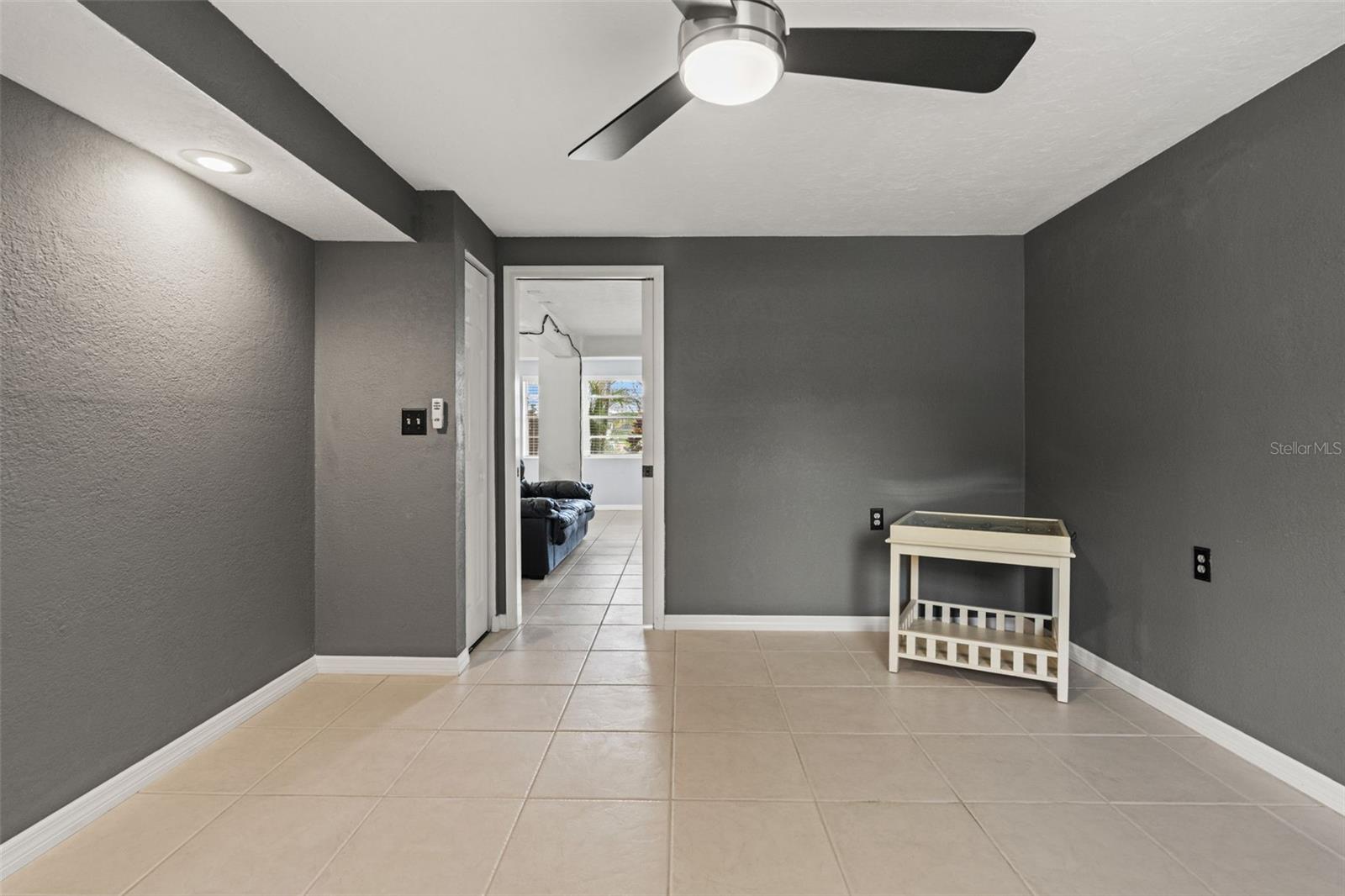 A second perspective highlights the room's open floor area, dark gray walls, and easy connection to the adjoining living space. The combination of natural light, closet storage, and separation from the main gathering area makes this a useful addition to the home's lower level.