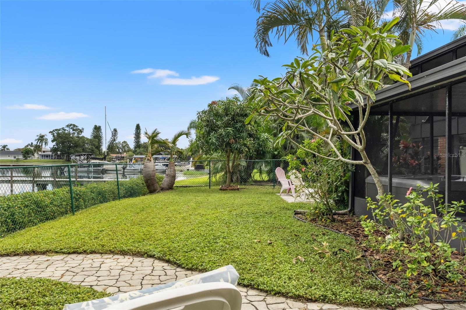 The waterfront backyard offers a lovely combination of open lawn, flowering plants, and mature tropical landscaping. With room to relax outdoors and views toward neighboring docks and boats, this setting makes the most of its lakeside location.
