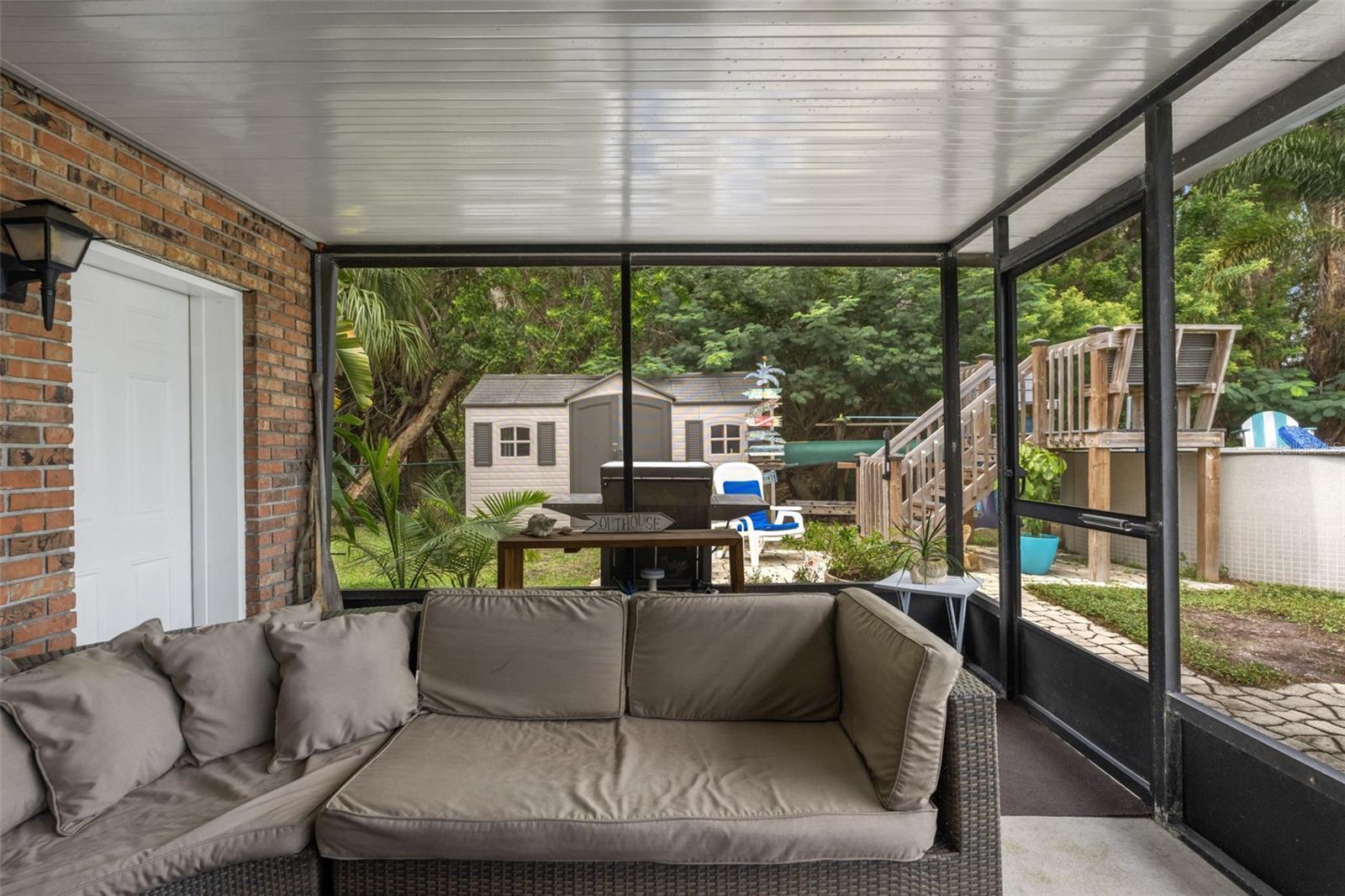 This covered, screened patio provides another comfortable outdoor gathering area, complete with sectional seating and access to the backyard. Beyond the enclosure, discover an above-ground pool, outdoor grilling area, and storage shed surrounded by mature trees.