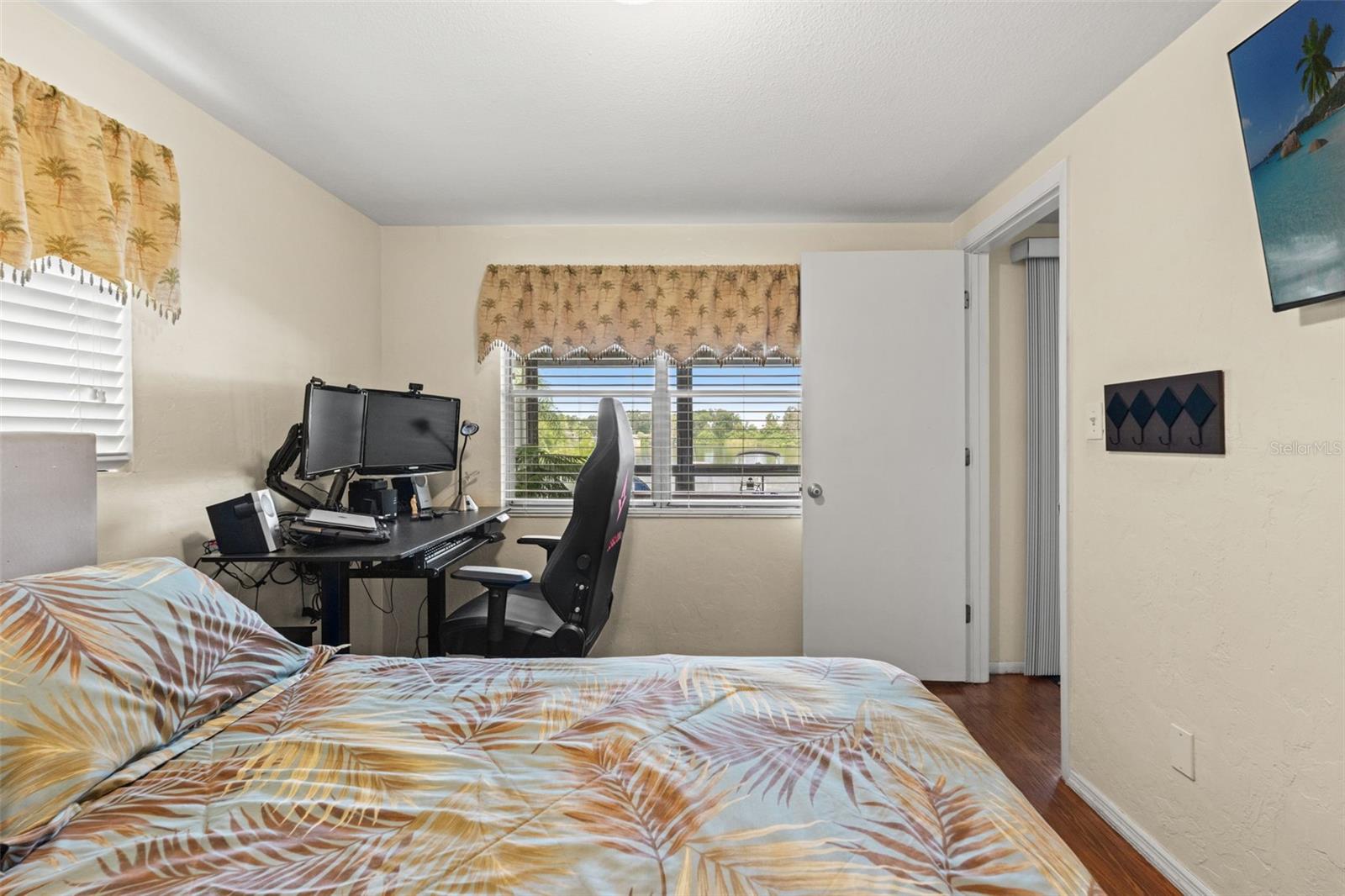 This versatile bedroom offers wood flooring, two windows for natural light, and a built-in closet. Currently arranged with both a bed and computer workstation, it demonstrates how easily the room accommodates sleeping and home office needs.