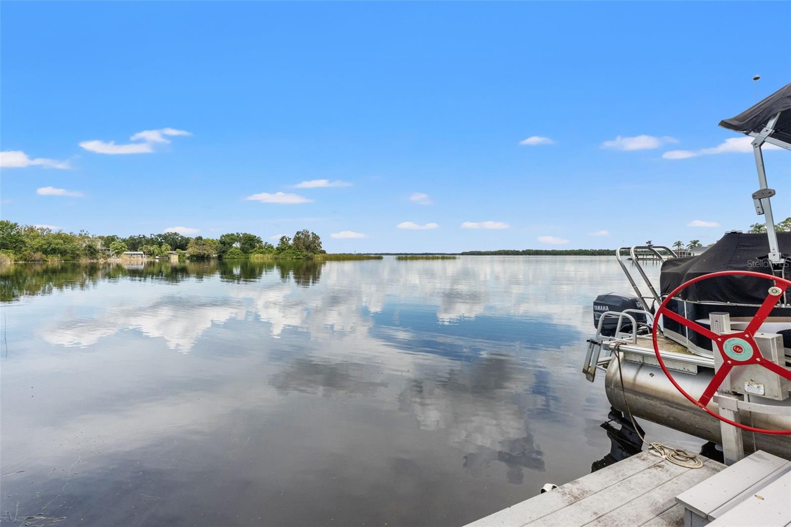 Beautiful reflections dance across the lake in this wide-open waterfront view. Natural vegetation along the shoreline adds to the peaceful setting, while the dock provides a front-row seat to the surrounding scenery.