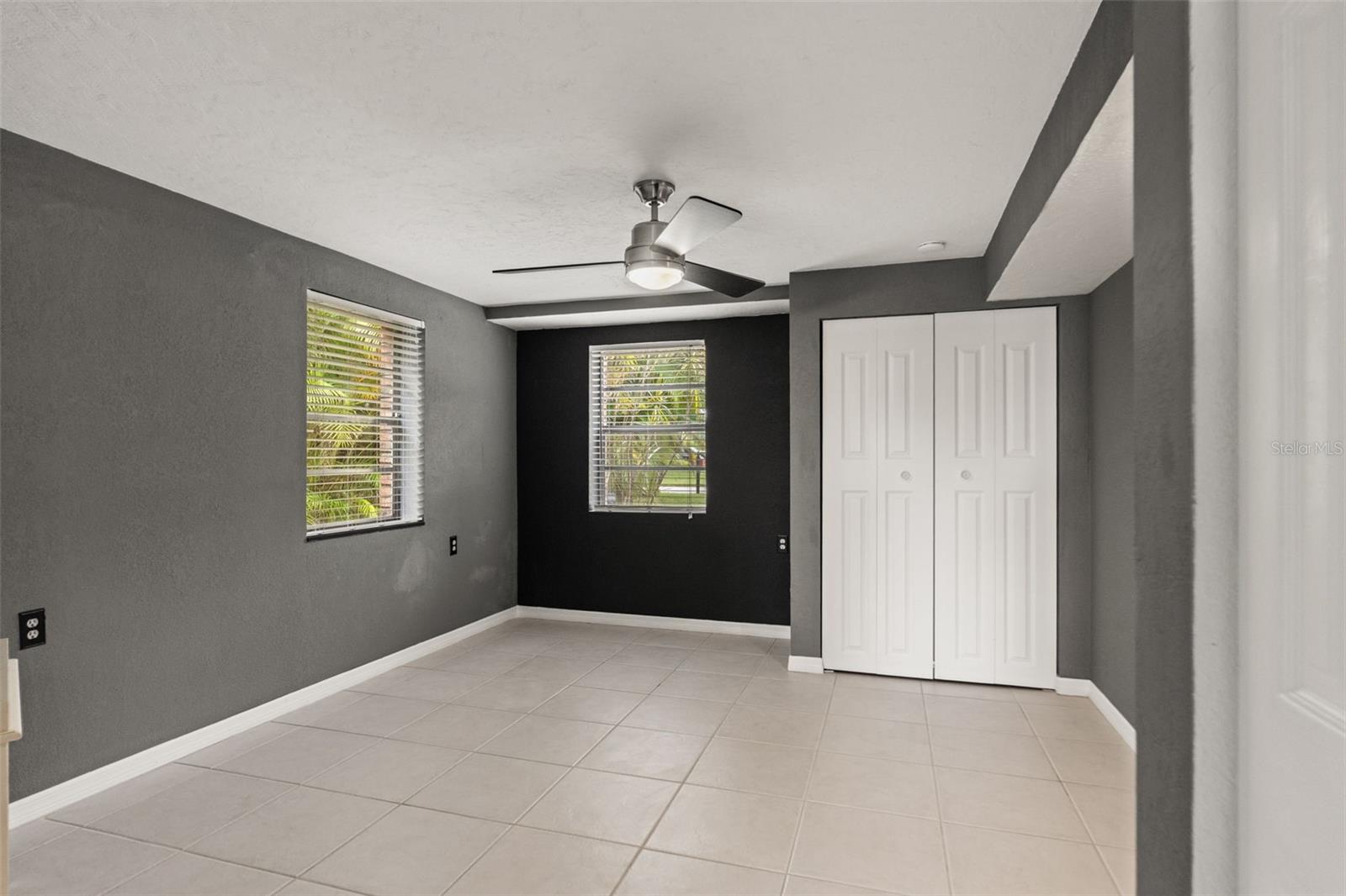 This separate downstairs room features neutral tile flooring, contemporary ceiling fan, two windows, and a closet. Its flexible layout provides options for a home office, hobby room, or additional guest space, depending on your needs.