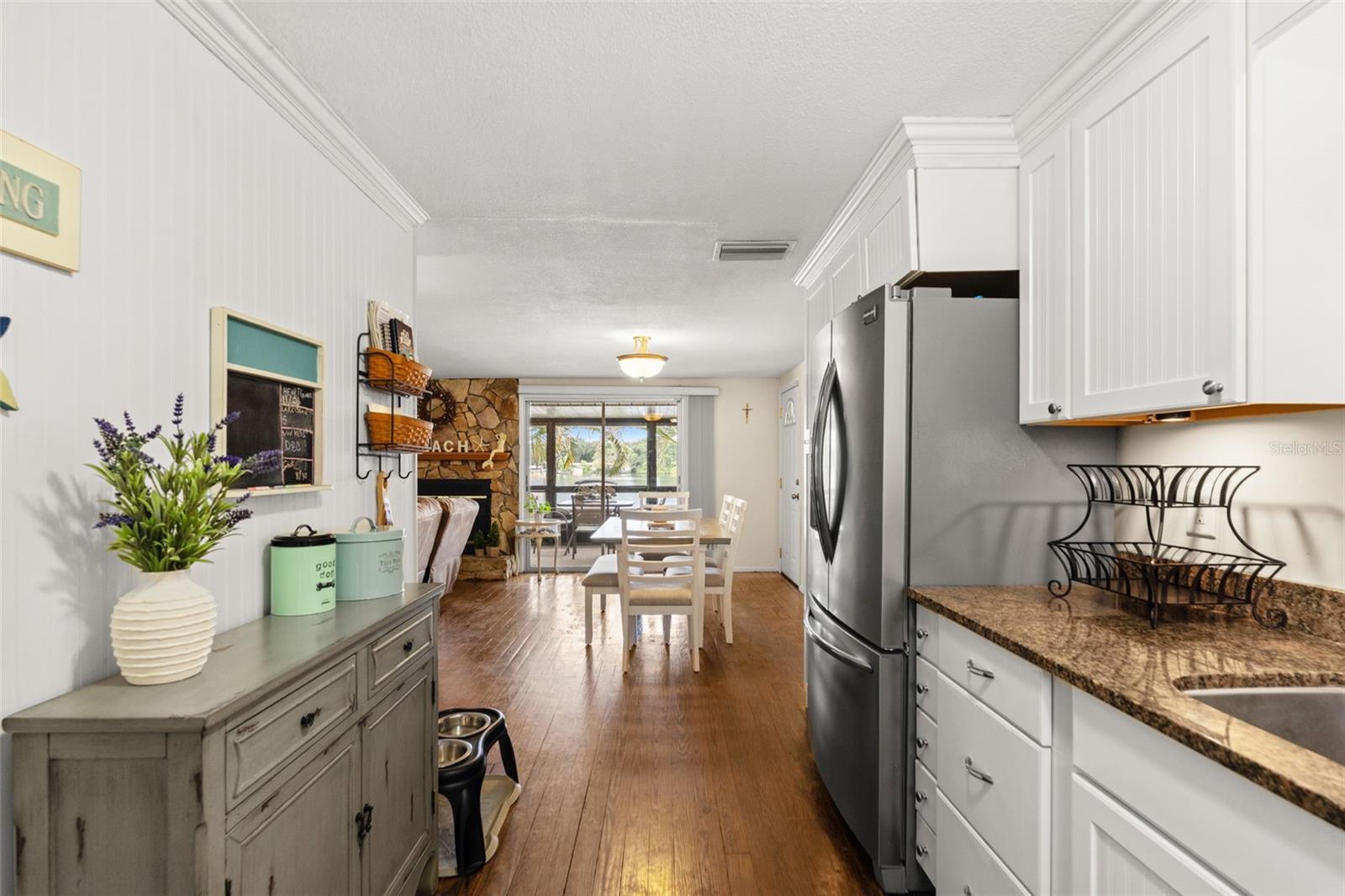 The kitchen opens directly to the dining and living areas, creating an easy flow throughout the upper level. White cabinetry, warm wood flooring, and a stainless steel refrigerator complement the home's relaxed coastal character.