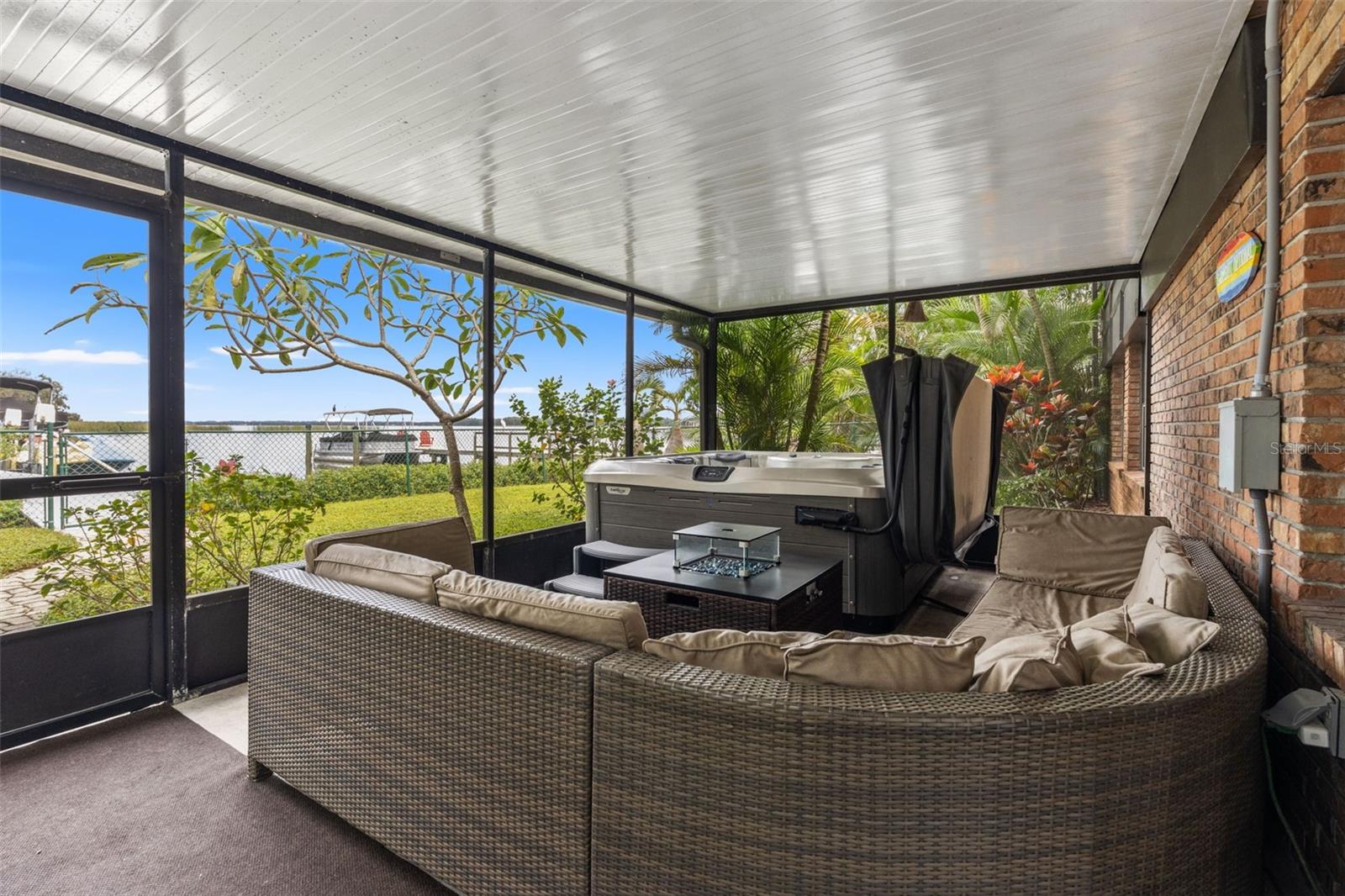 Your waterfront retreat continues downstairs! This spacious screened patio features a hot tub, comfortable sectional seating, and views toward the water. Surrounded by tropical landscaping, it's an inviting place to entertain or unwind after a day on the lake.