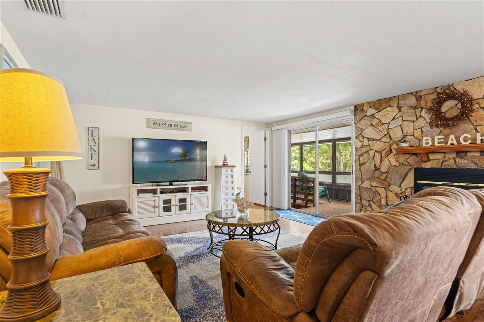 Comfortable, inviting, and full of character! The living room offers generous seating space, warm wood flooring, and direct access to a screened porch. The stone fireplace adds a cozy touch to this waterfront retreat.