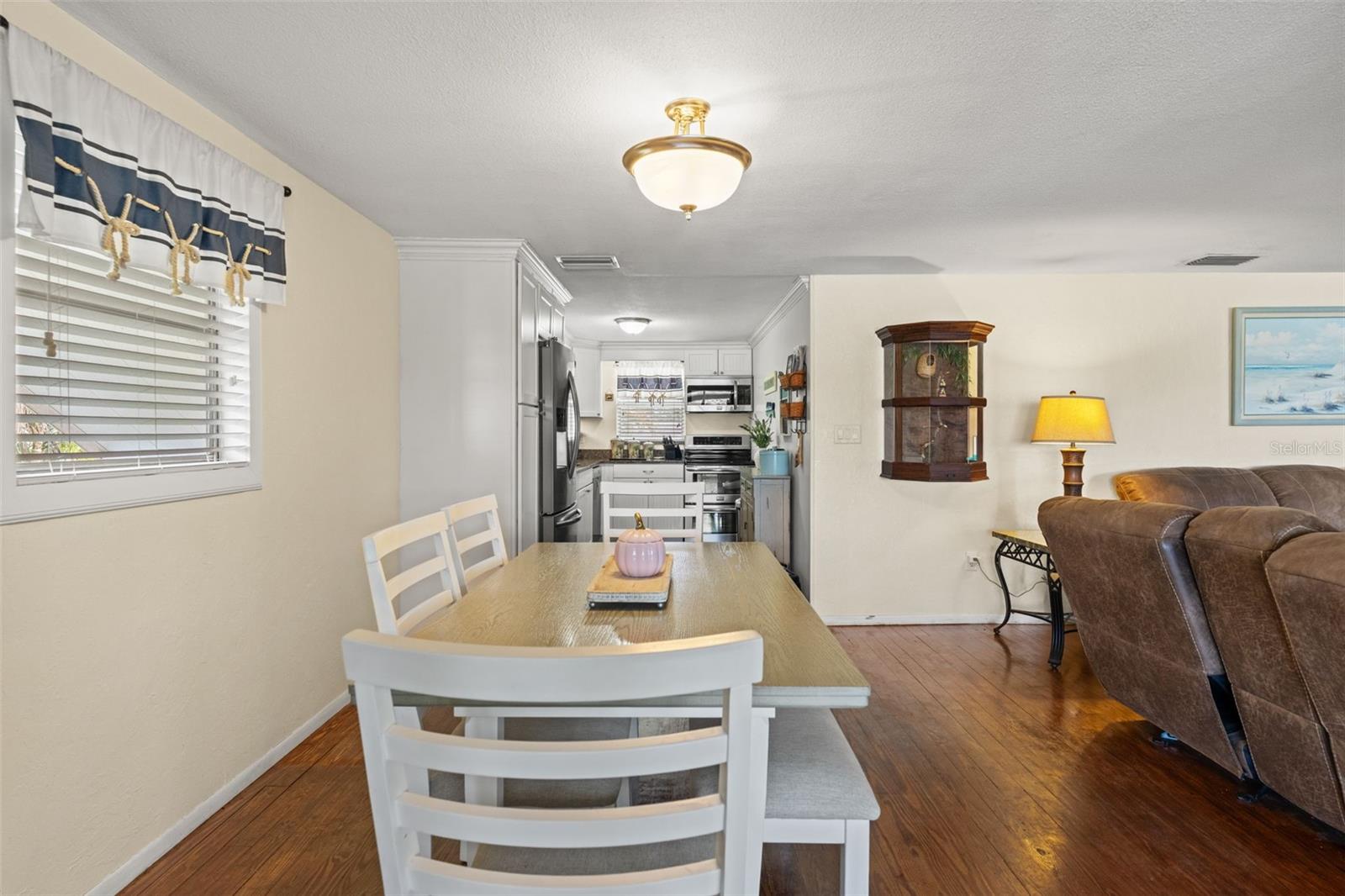The dining area sits conveniently between the kitchen and living room, making meals and gatherings easy. Wood flooring, soft neutral walls, and natural light create a comfortable, welcoming atmosphere.