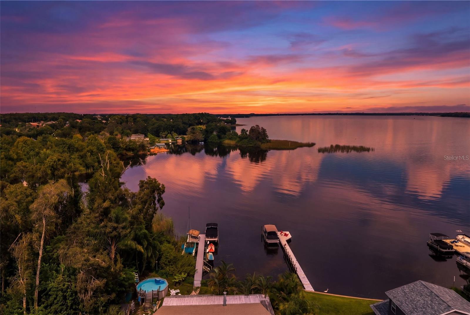 An incredible aerial perspective showcases the property's waterfront setting, private dock, and sweeping views across the water. With vibrant sunrise colors reflecting across the horizon, this is a spectacular backdrop for enjoying Florida's boating lifestyle.