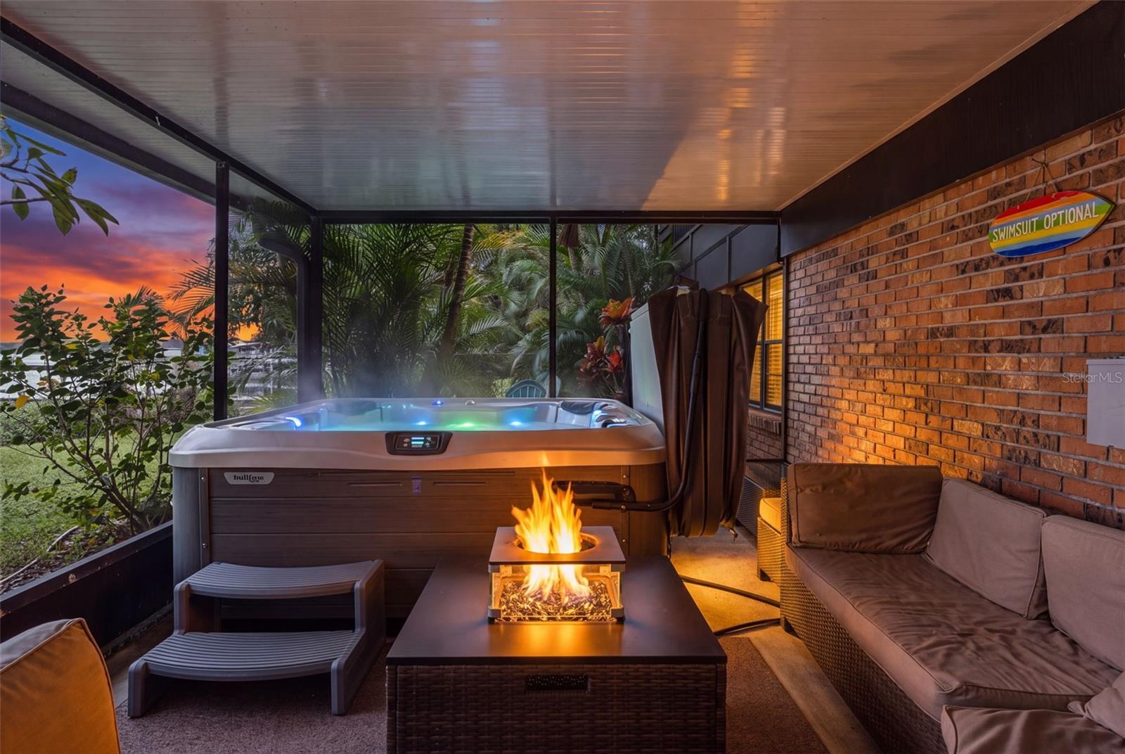 Your own private waterfront retreat! The screened patio features a bubbling hot tub, comfortable lounge seating, and a fire feature, all surrounded by lush tropical landscaping. Enjoy colorful sunrises over the water while relaxing in this inviting outdoor space.