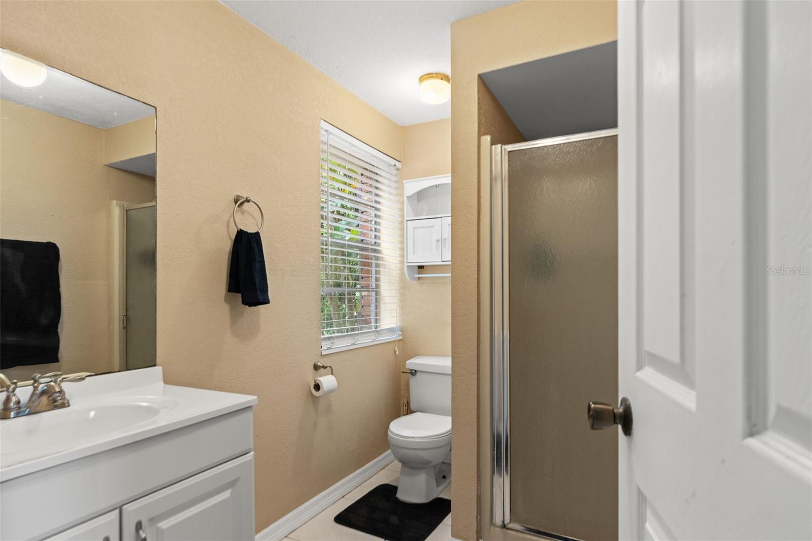 This lower-level bathroom features a white vanity, a walk-in shower with frosted glass enclosure, and a window that welcomes natural light. Conveniently located near the kitchenette and living area, it adds functionality to the home's flexible downstairs layout.