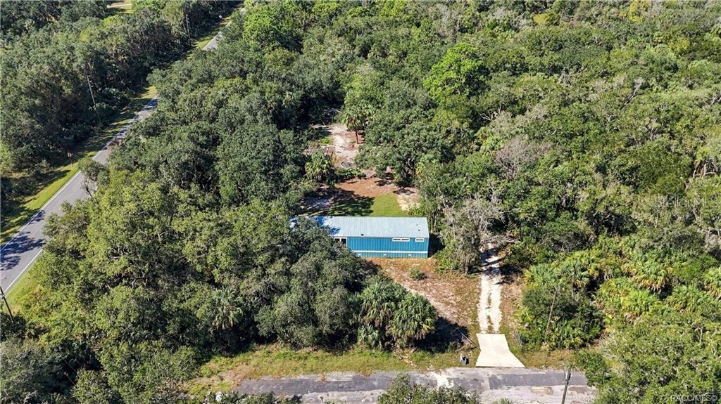 A BIRD'S-EYE VIEW! An aerial perspective showcases the home's wooded surroundings, natural landscape & driveway leading to the property.