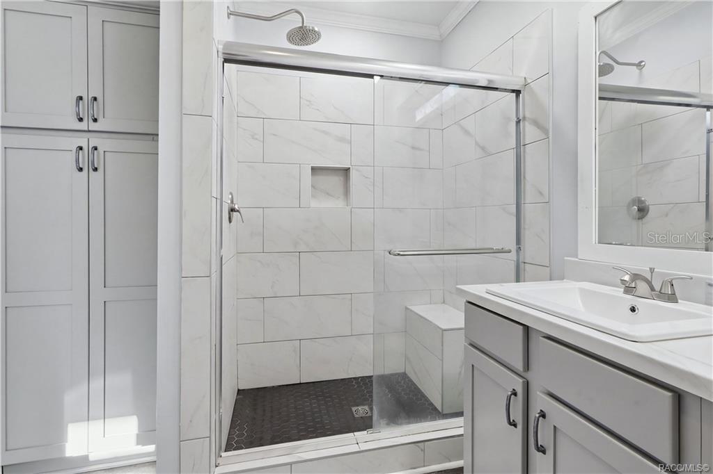 WALK-IN SHOWER features marble-look tile, a rainfall-style showerhead, glass sliding doors, built-in seating & a convenient recessed niche.