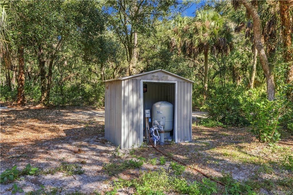 A PRACTICAL PROPERTY FEATURE! A separate enclosure houses the property's well equipment, surrounded by mature trees & natural vegetation.