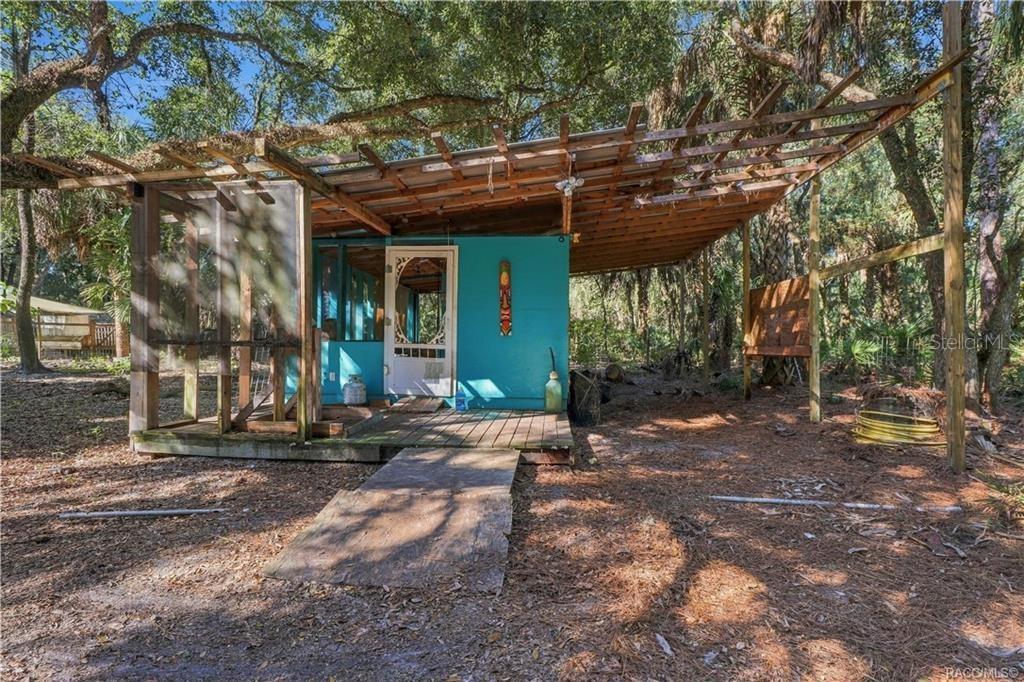 A UNIQUE OUTDOOR SPACE! A closer view of the rustic structure showcases its wooden deck, screened section & extended overhead framework.