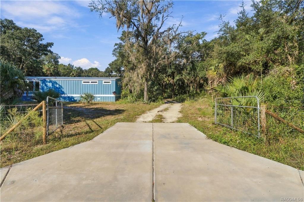 A GATED ENTRANCE WELCOMES YOU! The concrete driveway apron leads through a gated entrance into the 1.42 FULLY FENCED ACRES, offering space for vehicles & outdoor toys.