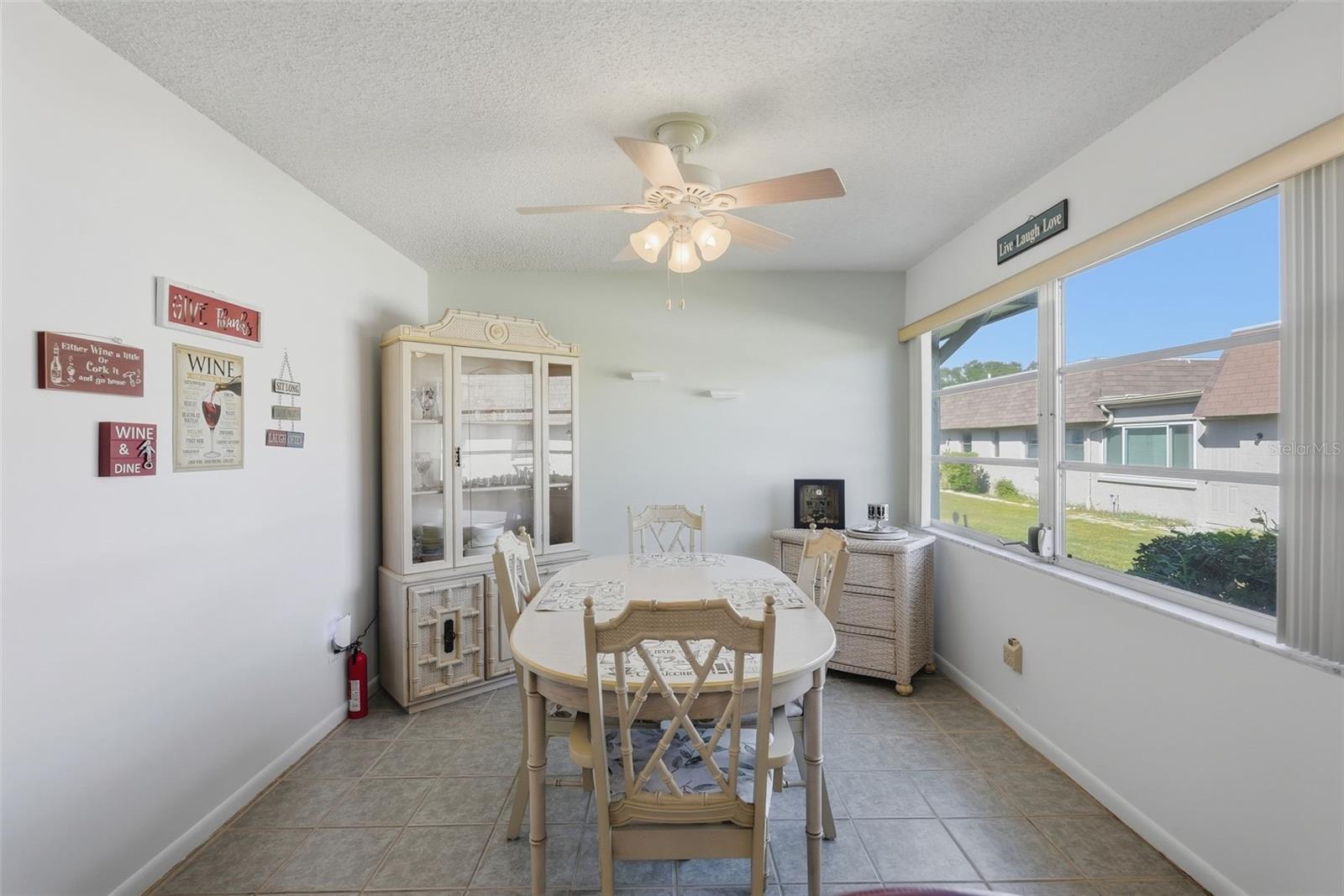 Sunny dining area with large windows and ceiling fan.