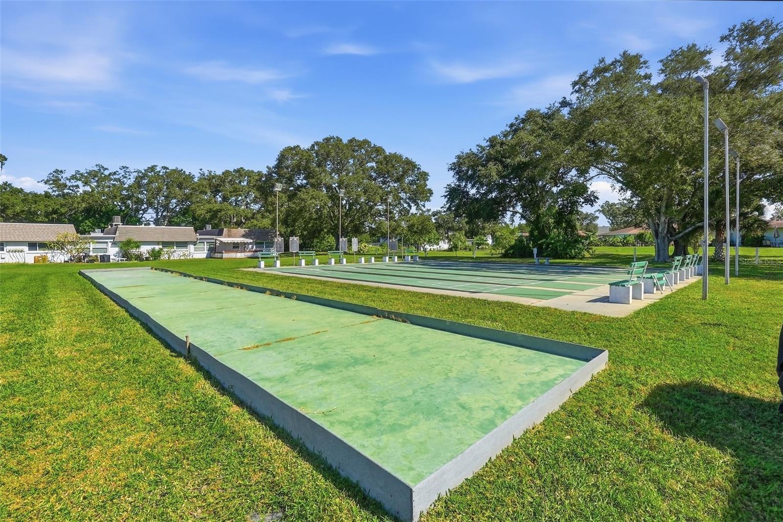 utdoor shuffleboard courts surrounded by mature trees and green space.