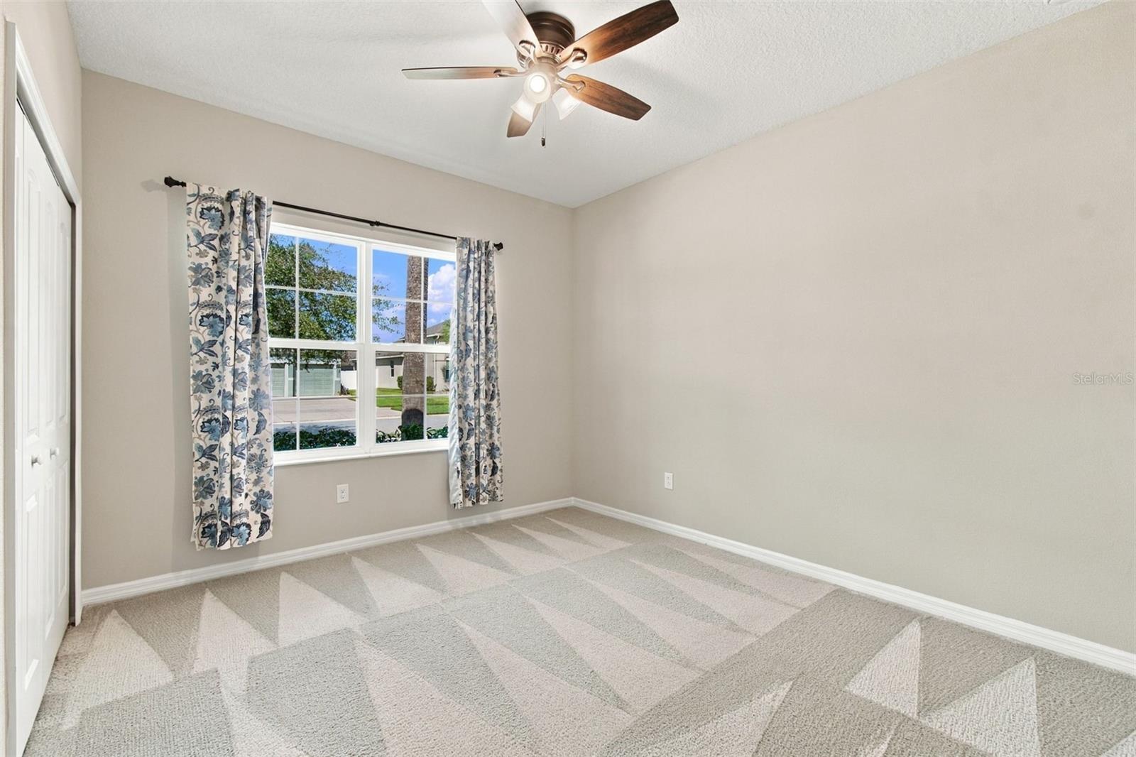 Guest bedroom with ceiling fan & large window facing the front yard