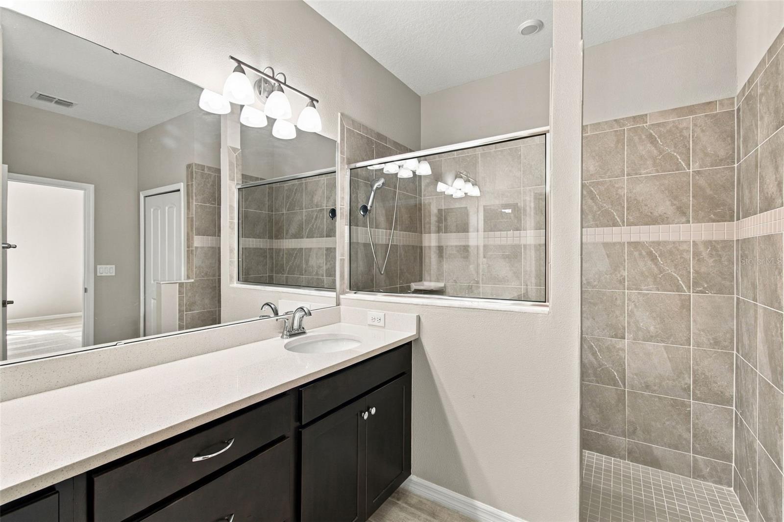 View of vanity and walk-in shower separated by half glass wall