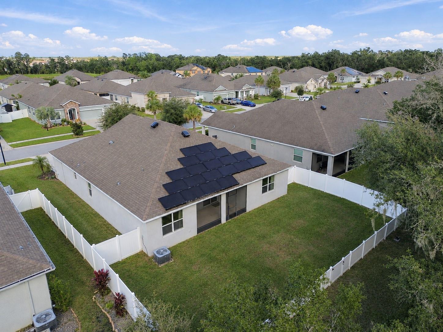 Overview of backyard and rear exterior of home by drone - solar panels and solar ventilation on roof