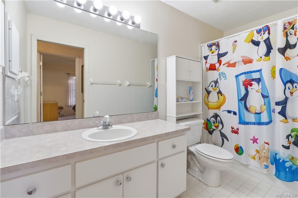 Guest bathroom with white cabinetry, extended vanity countertop, large wall mirror, and tub/shower combination.