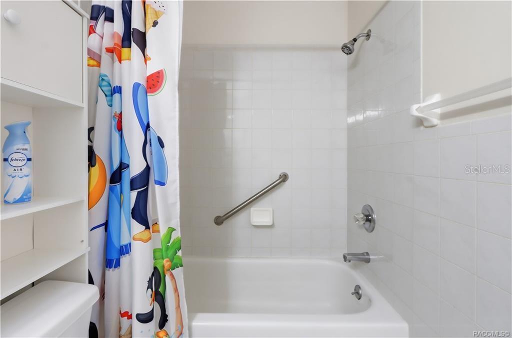 Tub/shower combination featuring white tile surround, built-in soap dish, and grab bar.