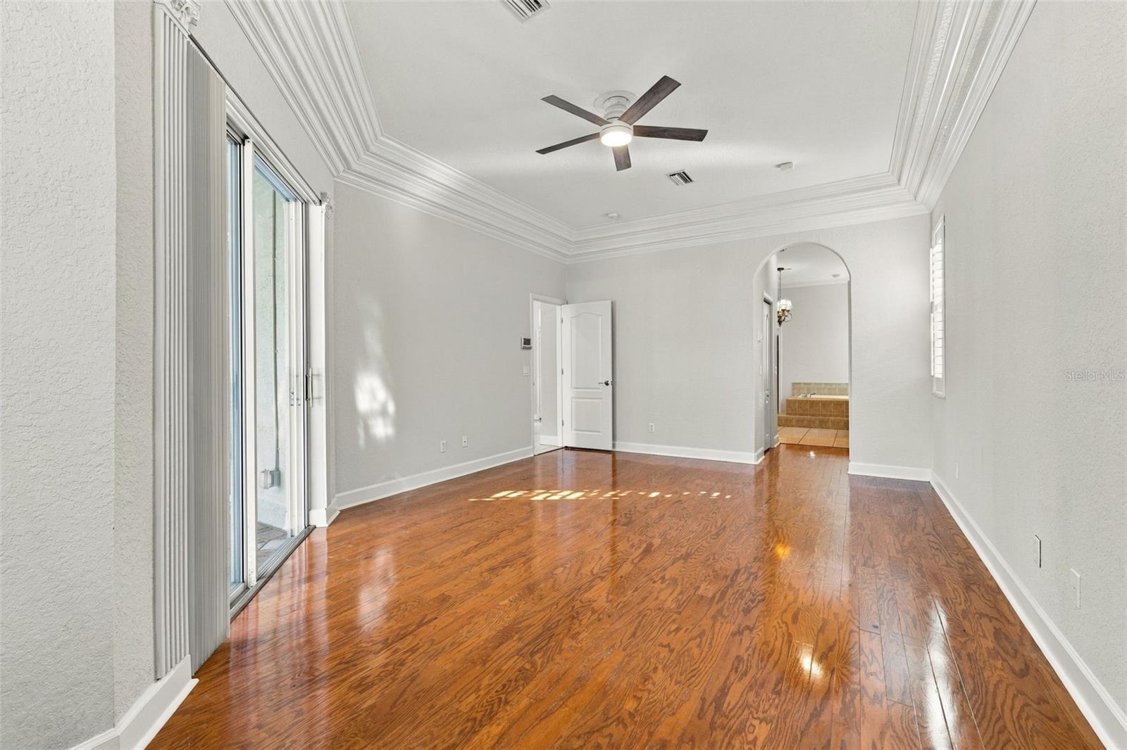 Primary Bedroom with Double Step Tray Ceiling adorned with Crown Molding, Sliding Glass Door to Pool/Spa area & Real Wood Floors!