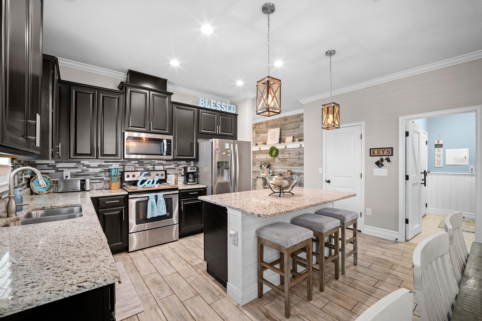Wide view of the kitchen with espresso cabinets, tile backsplash and pendant lights
