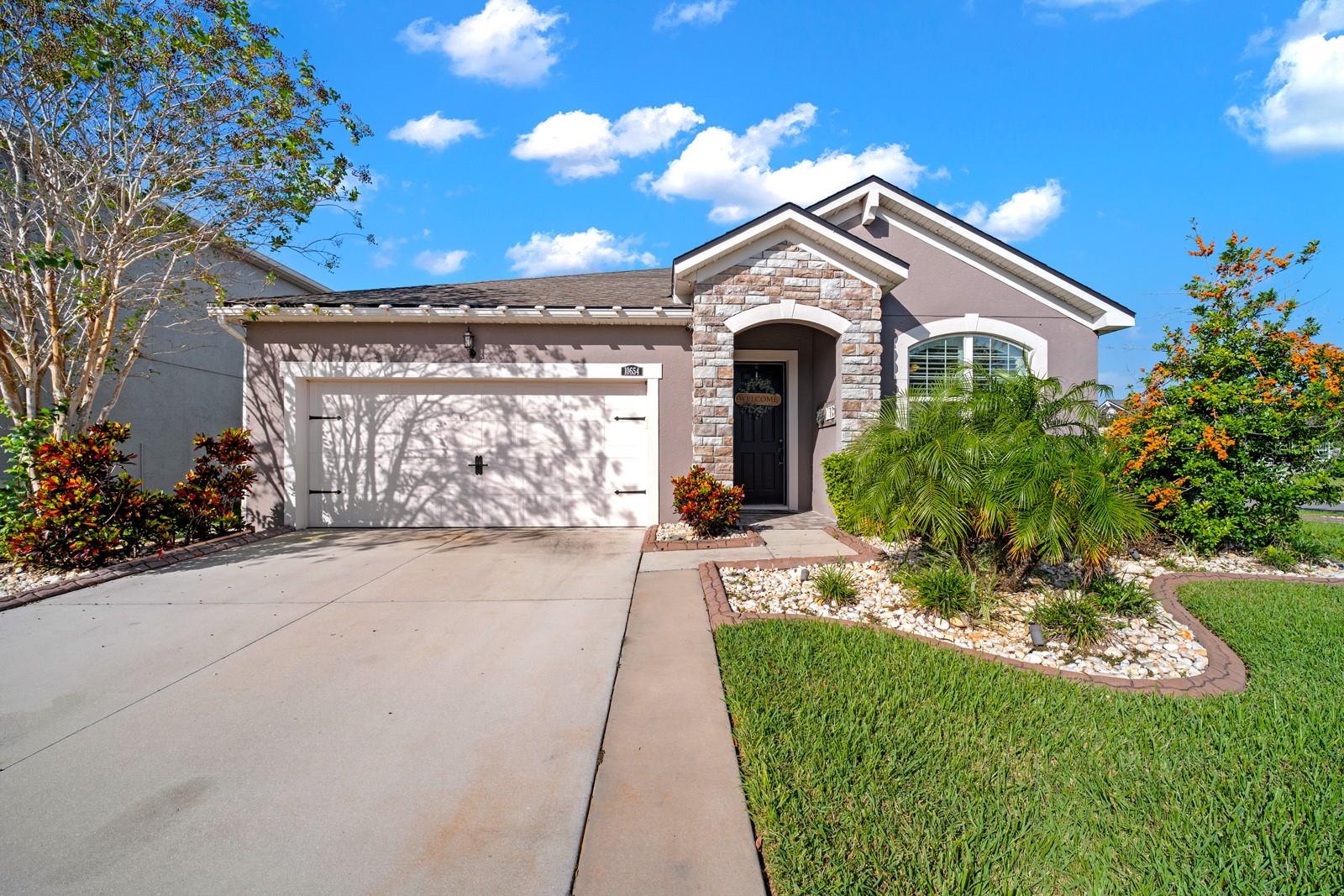 Front exterior with 2-car garage, stone accents and mature landscaping