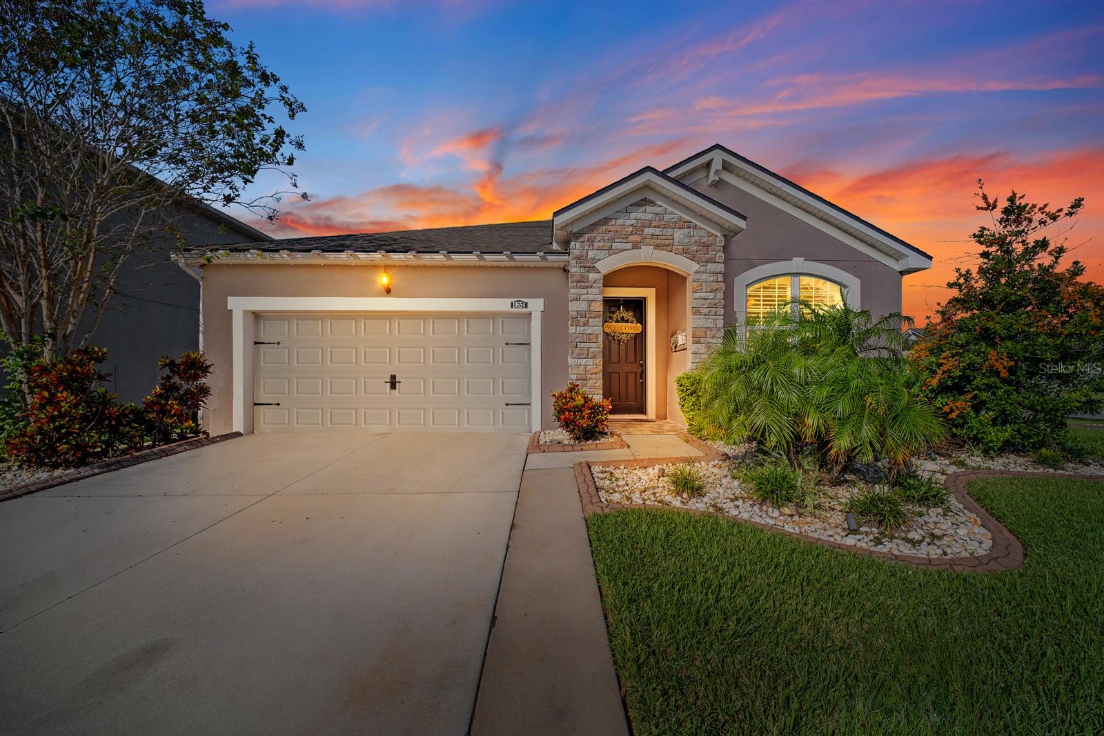 Front of the home at dusk with lit stone entry and landscaped front bed
