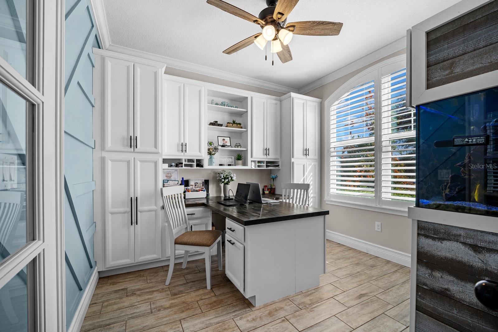 Office off the foyer with built-in cabinets, desk and plantation shutters