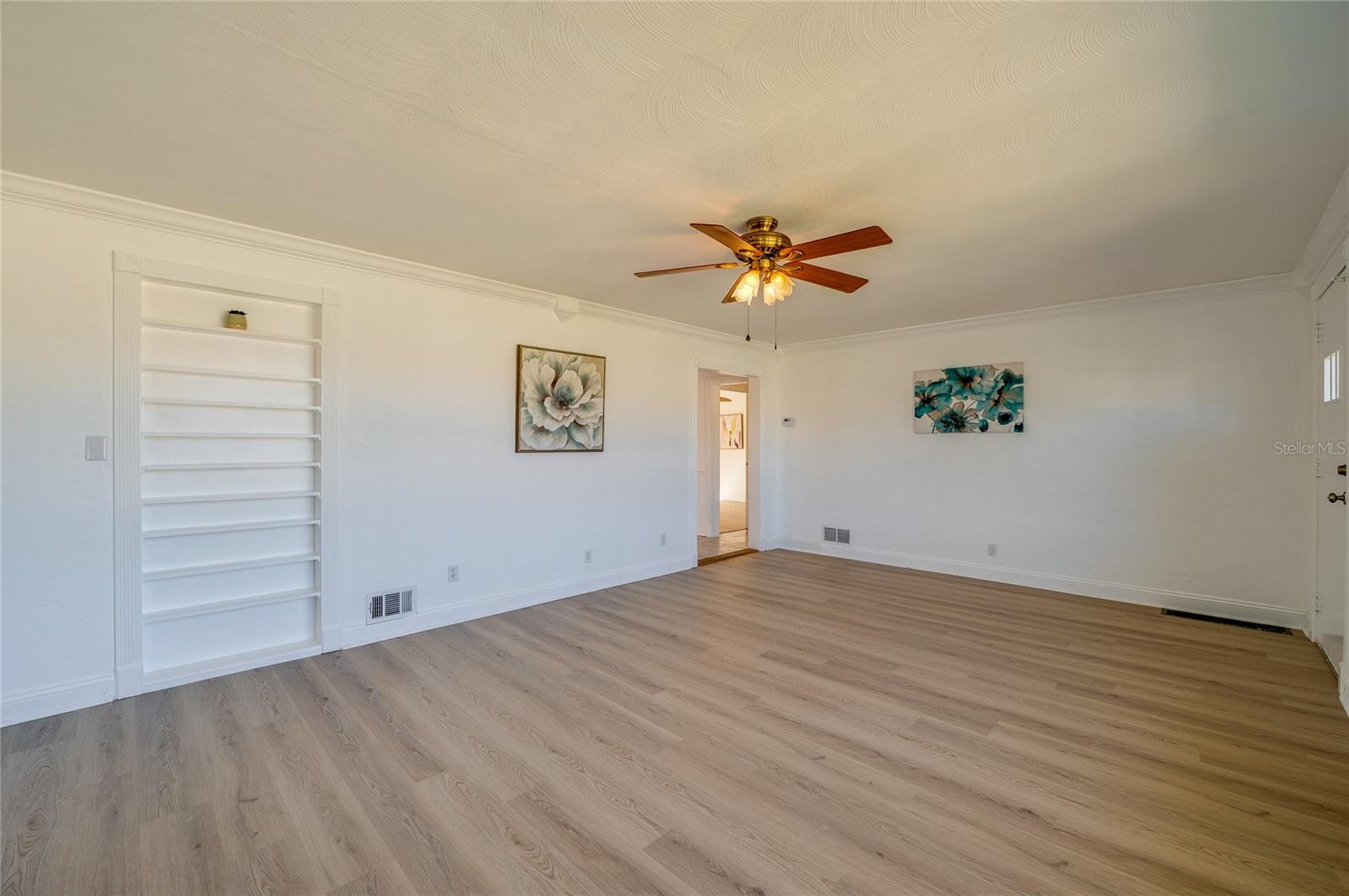 Open-concept living space framed by crisp white trim, continuous LVP flooring, and a built-in recessed wall shelving unit. The clean layout and central doorway provide an airy, connected atmosphere.