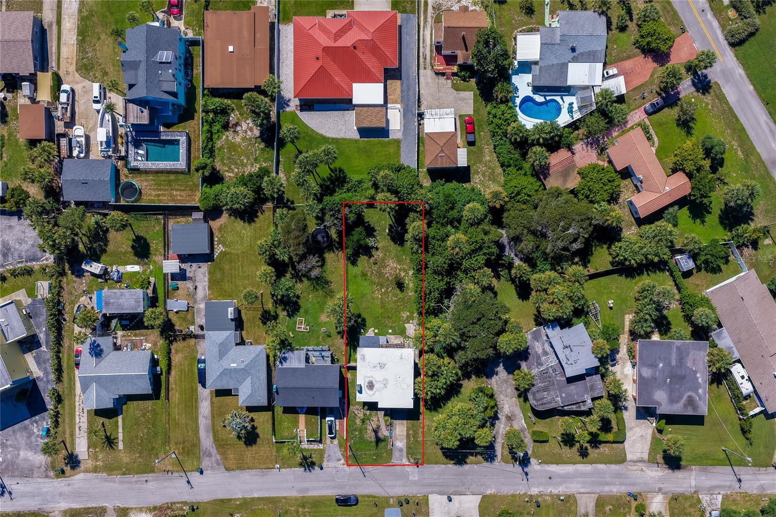 Direct overhead aerial view displaying the property boundaries outlined in red amidst a coastal residential neighborhood. Surrounding lots feature private swimming pools, lush palm trees, and detached garages.