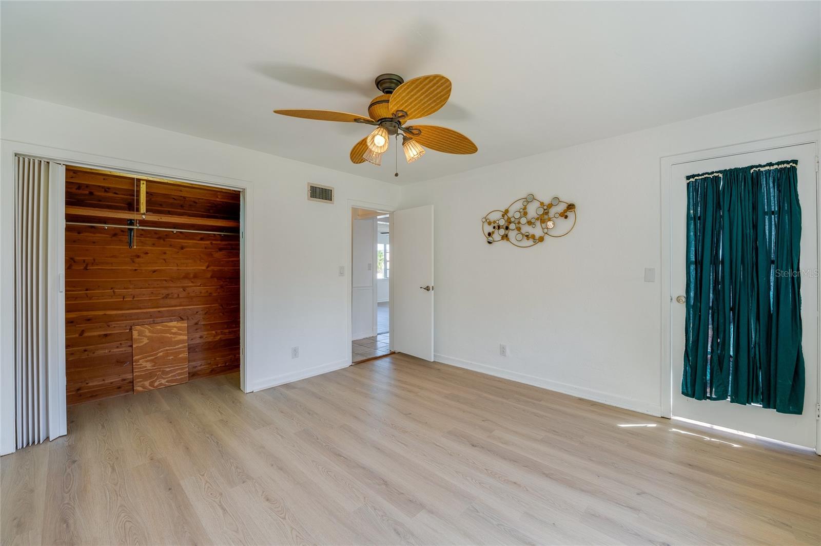 Versatile room displaying LVP flooring, a tropical-style ceiling fan, and a cedar-lined walk-in closet with built-in shelving. A glass-paneled exterior door with privacy drapery opens to an adjacent space.