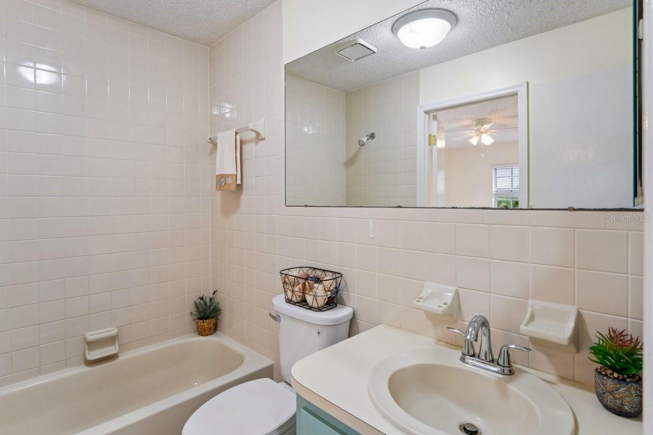 The bathroom features a tub with a shower and a single vanity, with access from both the bedroom and the living room.