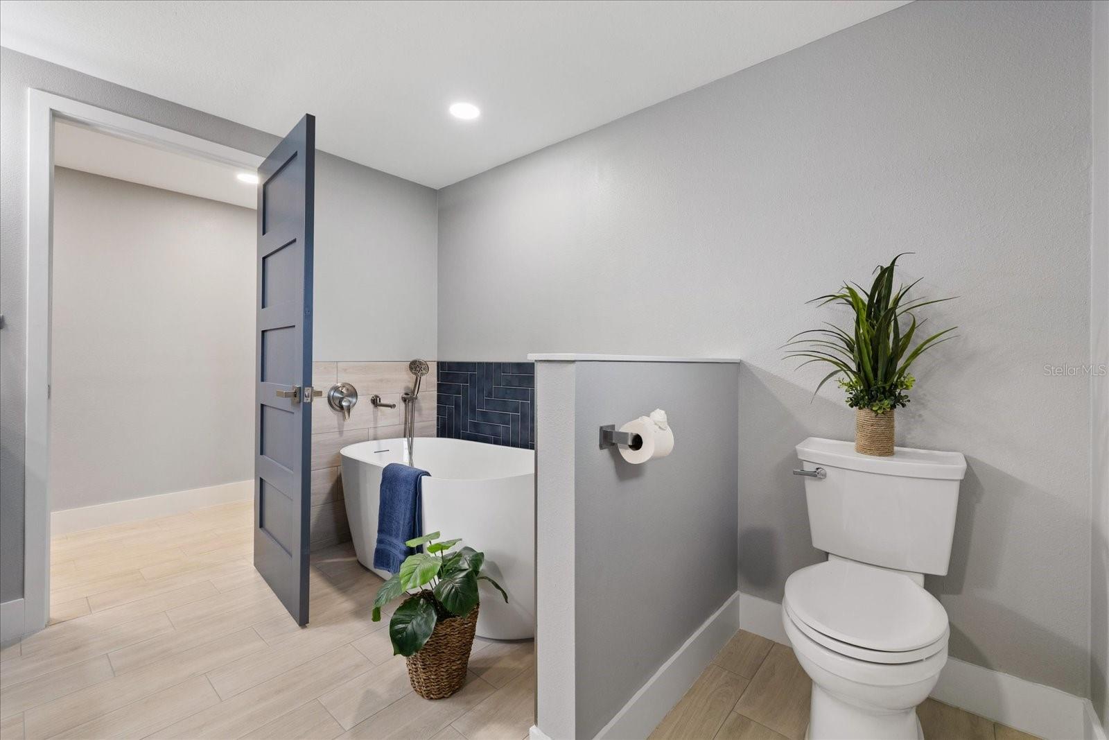 Opening to extra large walk in closet in primary bathroom with divided wall near tub