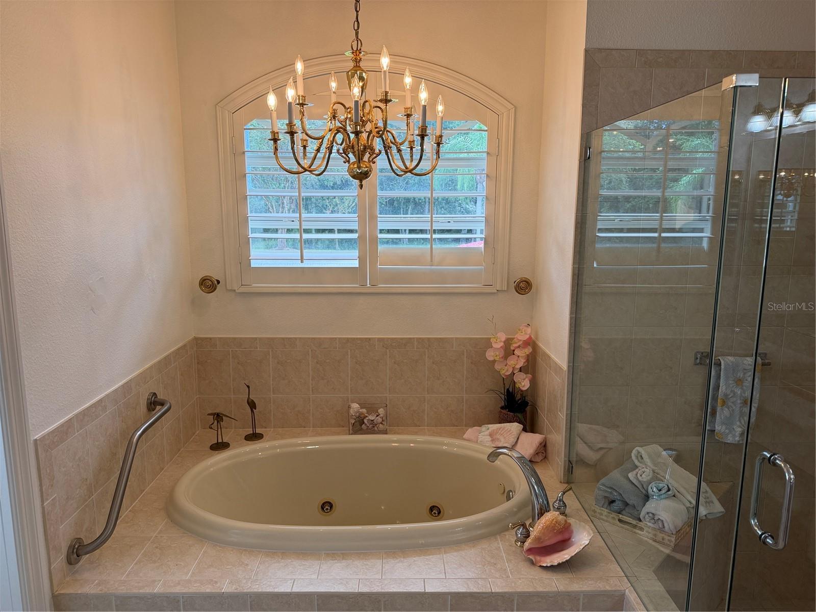 Jetted tub, chandelier, and plantation shutter in primary bathroom