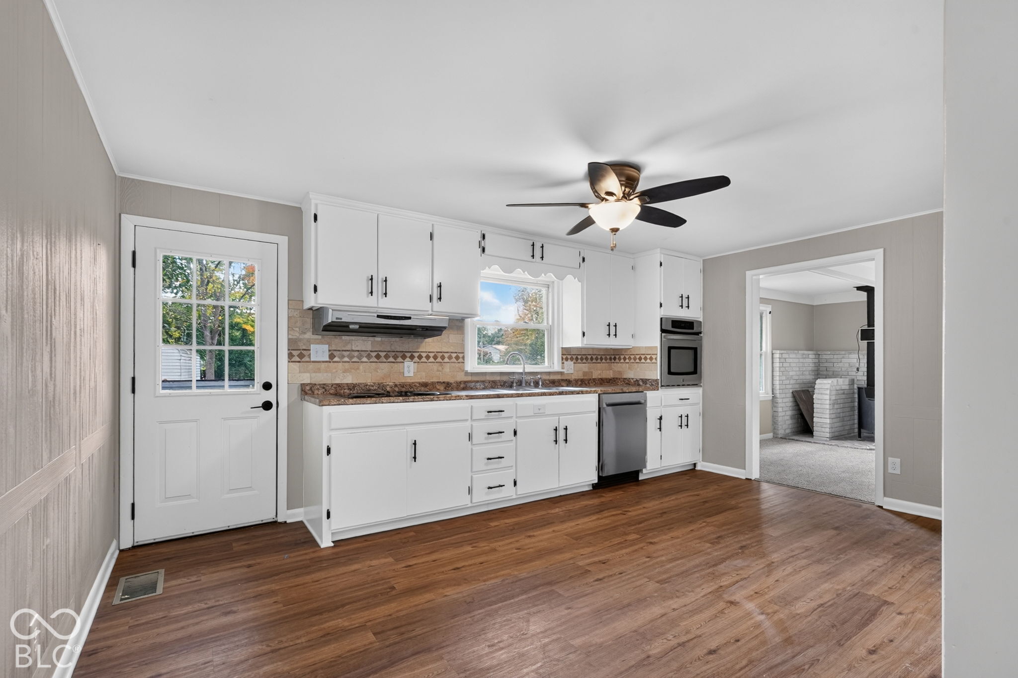 Kitchen featuring white cabinetry, wood-finish flooring, stone-pattern laminate countertops, tiled backsplash, and stainless steel dishwasher