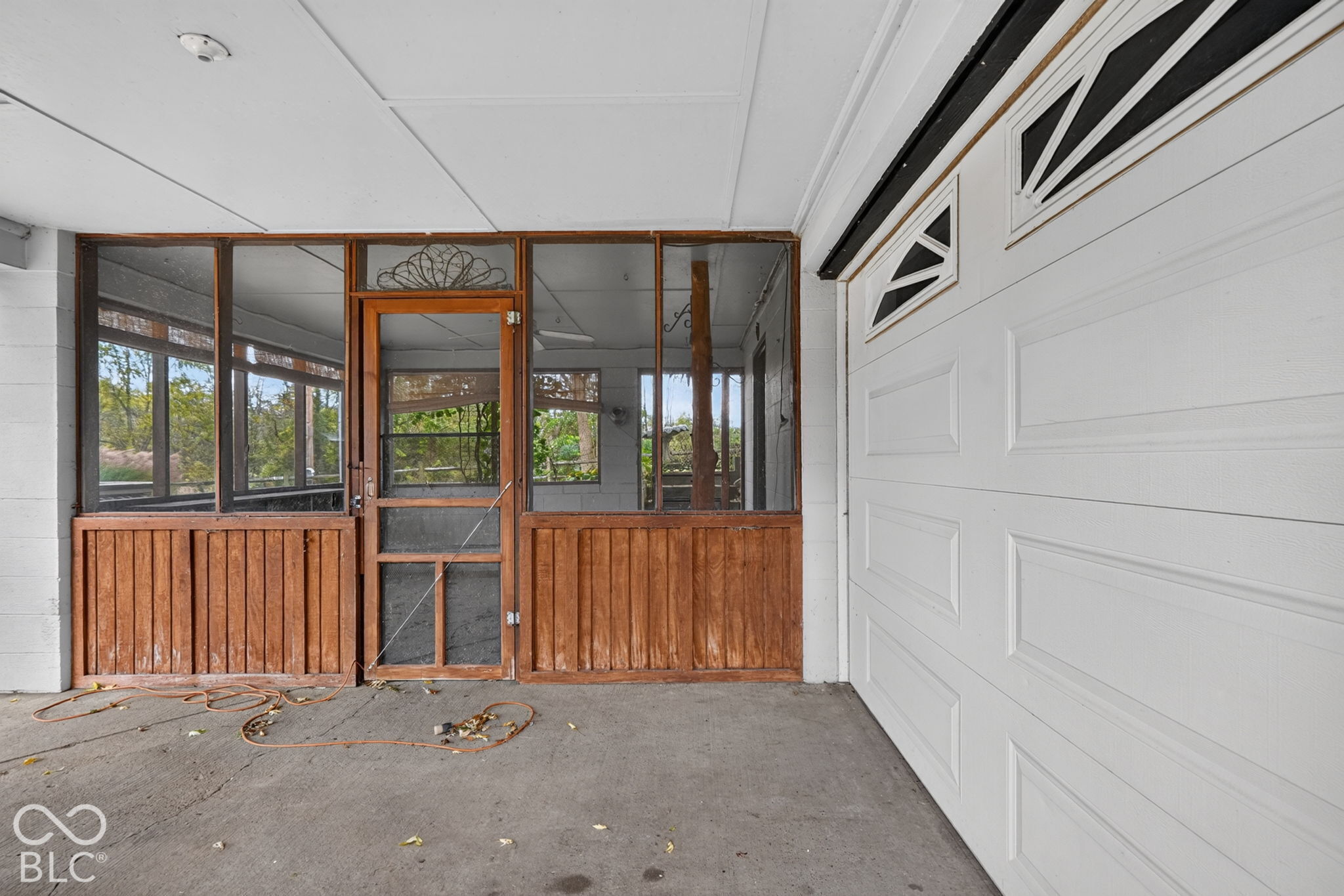 Covered entryway featuring a white overhead garage door and a screened-in porch with wood-panel wainscoting and a decorative screen door