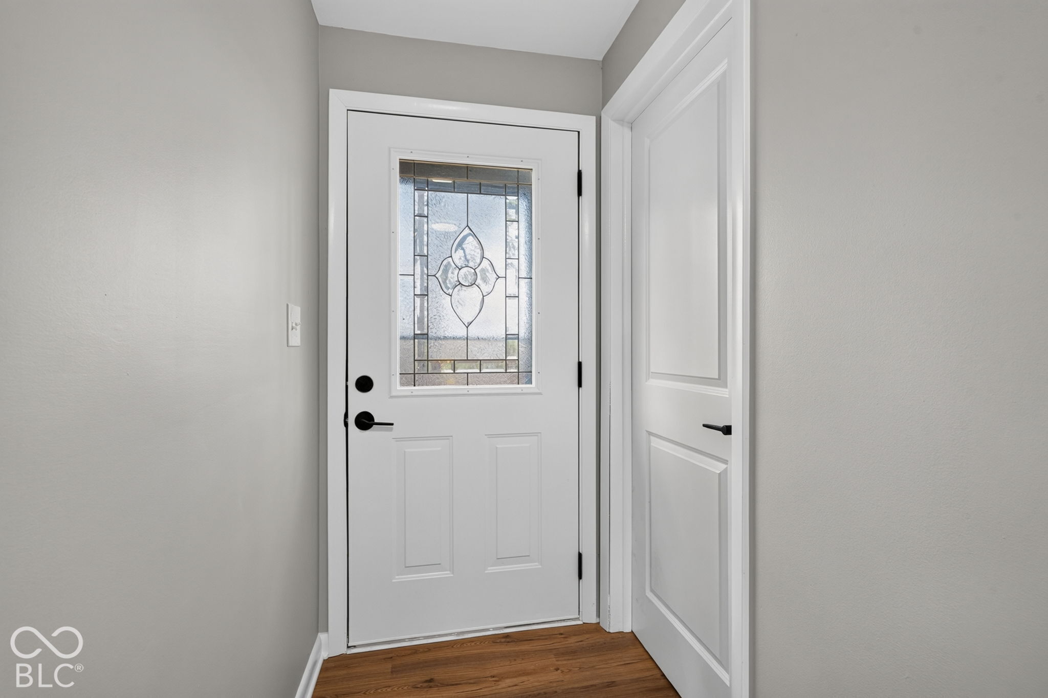 Entry door featuring a decorative glass insert, complemented by matte black hardware and wood-finish flooring