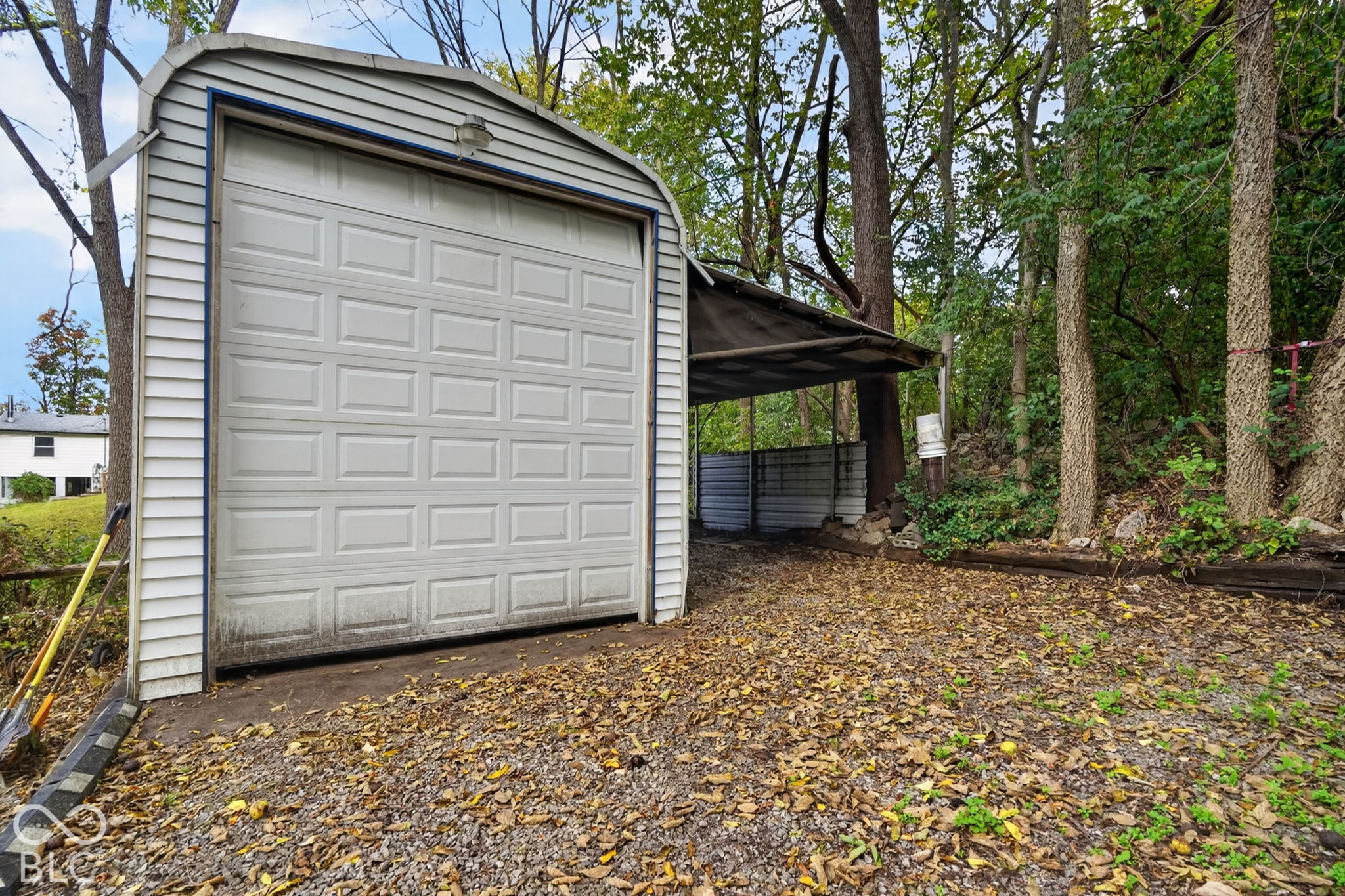 Detached structure featuring a vinyl-sided exterior, a single overhead garage door, and a metal-roofed side carport