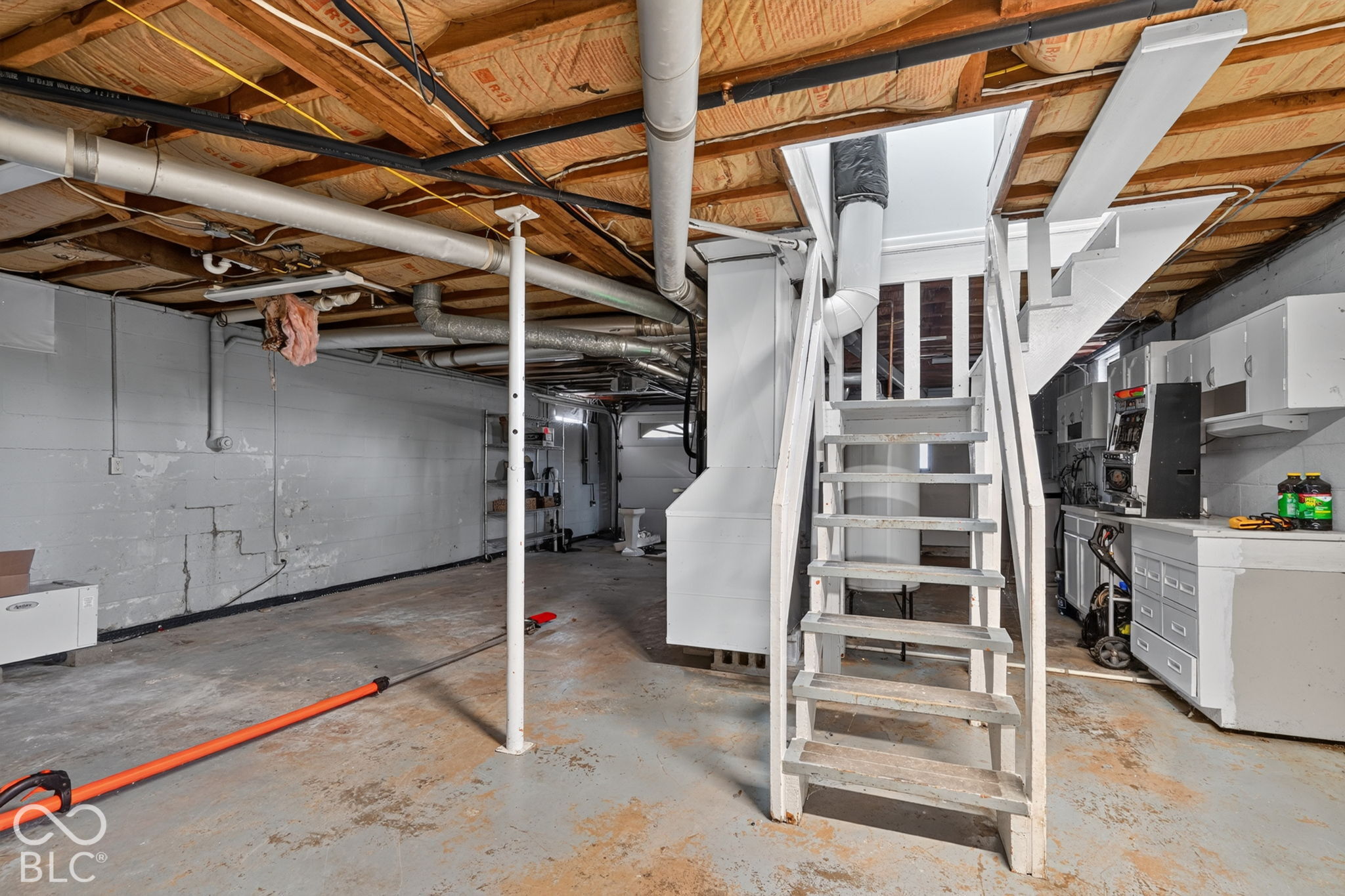 Unfinished lower level featuring concrete flooring, painted masonry walls, exposed ceiling joists, and built-in cabinetry with a countertop