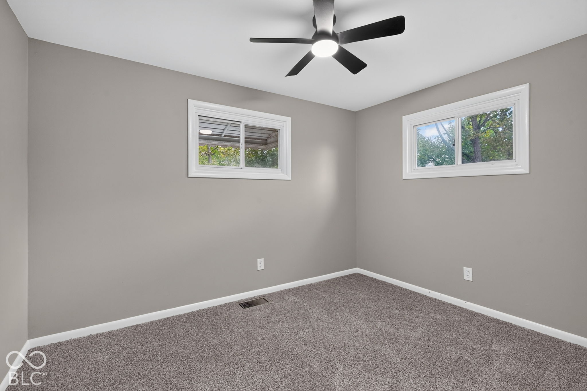 Neutral interior room with plush carpeting, dual sliding windows, and a matte black ceiling fan with integrated lighting