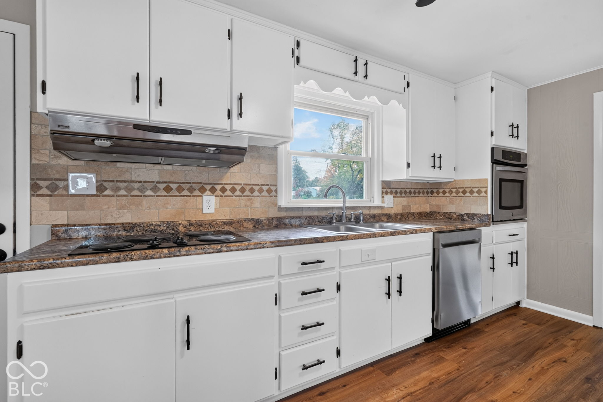 Kitchen featuring white cabinetry with matte black hardware, stone-tile backsplash, laminate countertops, wood-finish flooring, and stainless steel appliances