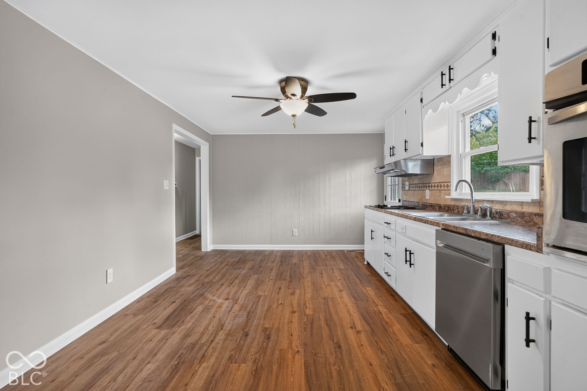 Kitchen featuring wood-finish flooring, white cabinetry with matte black hardware, stainless steel dishwasher, built-in wall oven, and a ceiling-mounted light fixture with fan