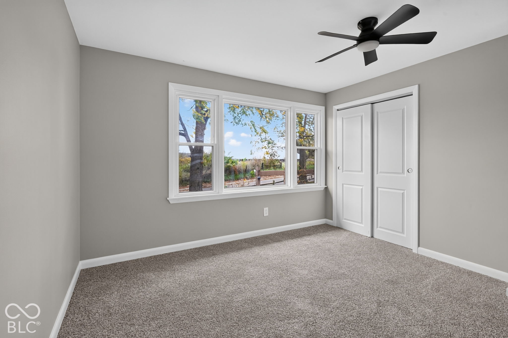 Neutral-toned bedroom featuring wall-to-wall carpeting, a multi-pane window assembly, matte black ceiling fan, and double-panel closet doors